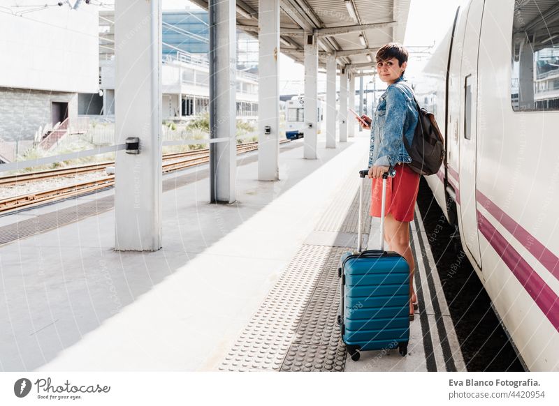junge Backpacker kaukasische Frau hält Gepäck am Bahnhof bereit, den Zug zu fangen. Hält das Mobiltelefon und benutzt eine App. Reisen Konzept Handy reisen