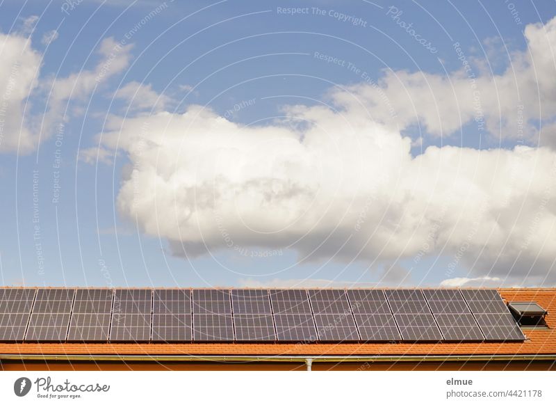 Auf dem roten Ziegeldach, neben einem Dachfenster wurden Sonnenkollektoren installiert / Dekowolken / Ökostrom / Photovoltaikanlage Energiewende Klimawandel