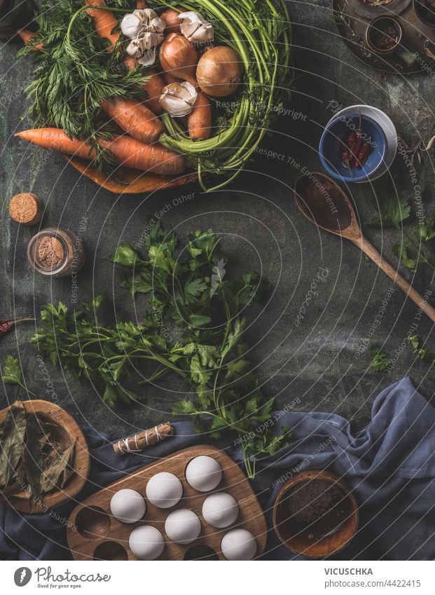 Gesunde Zutaten für eine schmackhafte Küche zu Hause. Frisches Gemüse und Kräuter auf einem dunklen Küchentisch mit einem Holzlöffel, frischen Eiern und getrockneten Gewürzen. Ansicht von oben