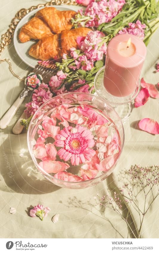 Glaswasserschale mit rosa Blumen auf Picknickdecke mit Croissants und Kerzen. Sonniger Tag. Ästhetisches Picknick-Konzept Wasser Schalen & Schüsseln Decke