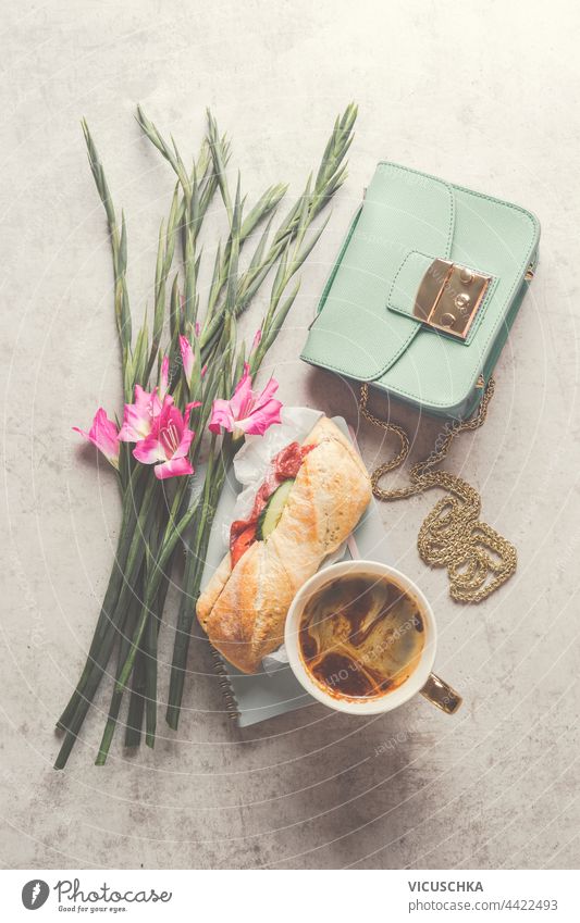 Niedliches ästhetisches Frühstück oder Mittagessen mit Kaffee und Sandwich, daneben ein Blumenstrauß und eine kleine Frauenhandtasche. Ansicht von oben niedlich