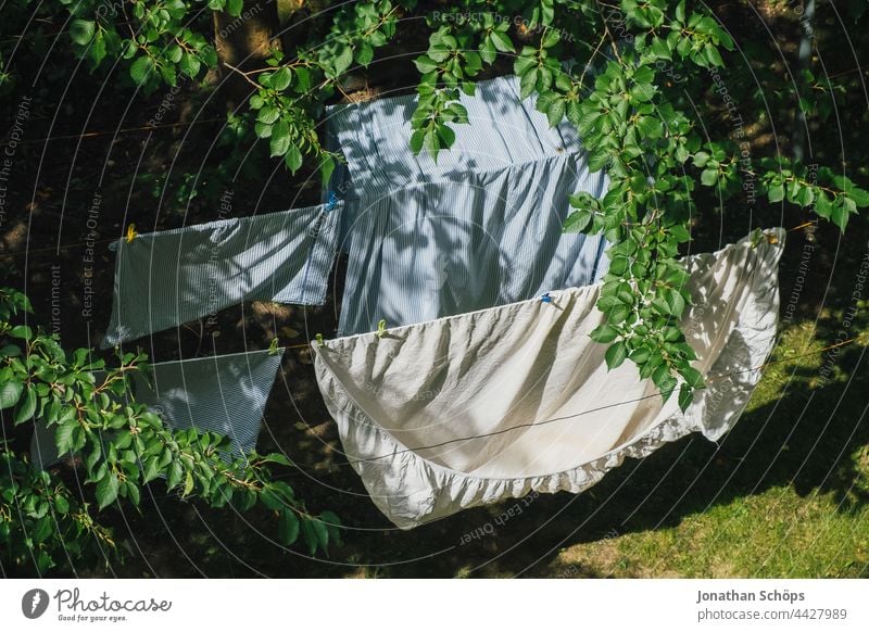 Bettwäsche beim Trocknen auf der Wäscheleine draußen im Garten wäsche aufhängen Wäsche trocknen Wind Hof Hinterhof Wiese Baum Zweige Äste Leine Bettbezug