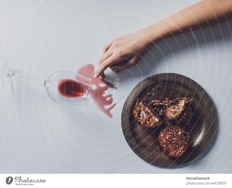 Ein Arm, ein Teller mit Granatäpfeln und ein Glas Wein auf einem Tisch verschüttet Hand Finger Frau Mensch Farbfoto Innenaufnahme Arme Granatapfel Schatten