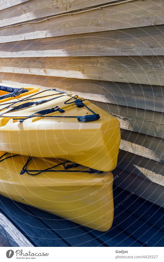zwei gelbe Kajaks gestapelt neben einer Holzwand Plastik Farbfoto Außenaufnahme Wasser Sport Wassersport Menschenleer Tag Ferien & Urlaub & Reisen