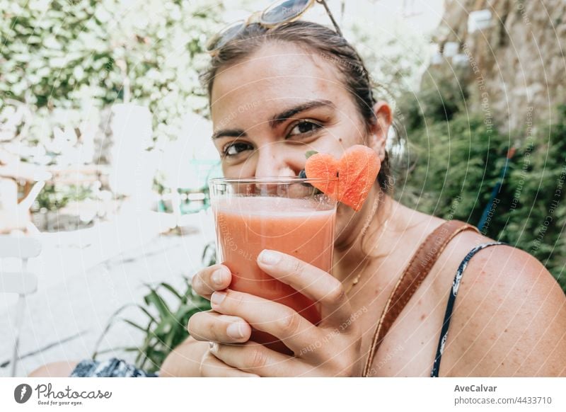 Frau lächelt in die Kamera, während sie ein frisches Sommergetränk in einem Garten hält und sein Gesicht mit dem Getränk bedeckt, Sommerferienkonzept Porträt