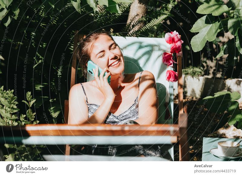 Frau lachend beim Telefonieren in einem sonnigen Garten während der Ferien, entspanntes Arbeiten von zu Hause aus Mitteilung Anschluss Handy Zeit