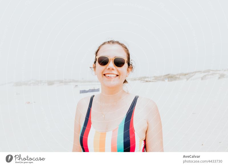 Junge Frau in einem Badeanzug und Sonnenbrille lächelt in die Kamera während eines sonnigen Tages am Strand, Freiheit und Urlaub Konzept, Porträt Spaß
