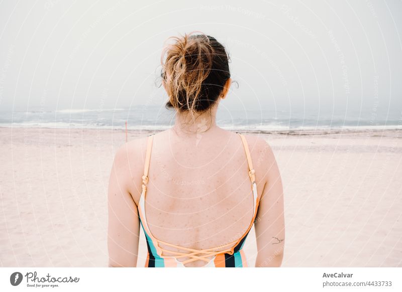Rücken einer jungen Frau im Badeanzug, melancholischer Strand, Urlaub, Nachsommerstimmung Spaß Badebekleidung Emotion eine Person Anzug sorgenfrei Sonnenbad