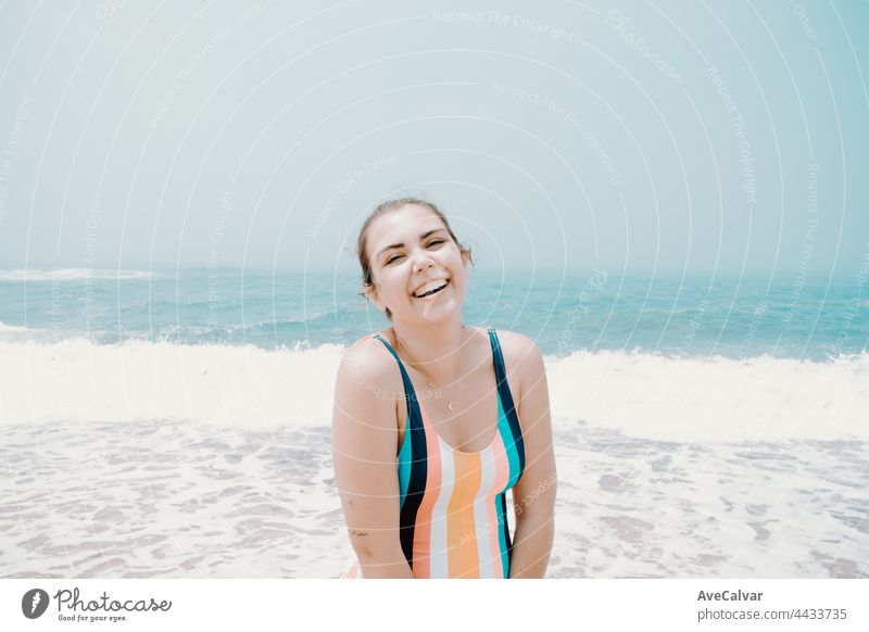 Junge Frau in einem Badeanzug lacht in die Kamera während eines sonnigen Tages am Strand mit dem Meer als Hintergrund, Freiheit und Urlaub Konzept, Kopie Raum