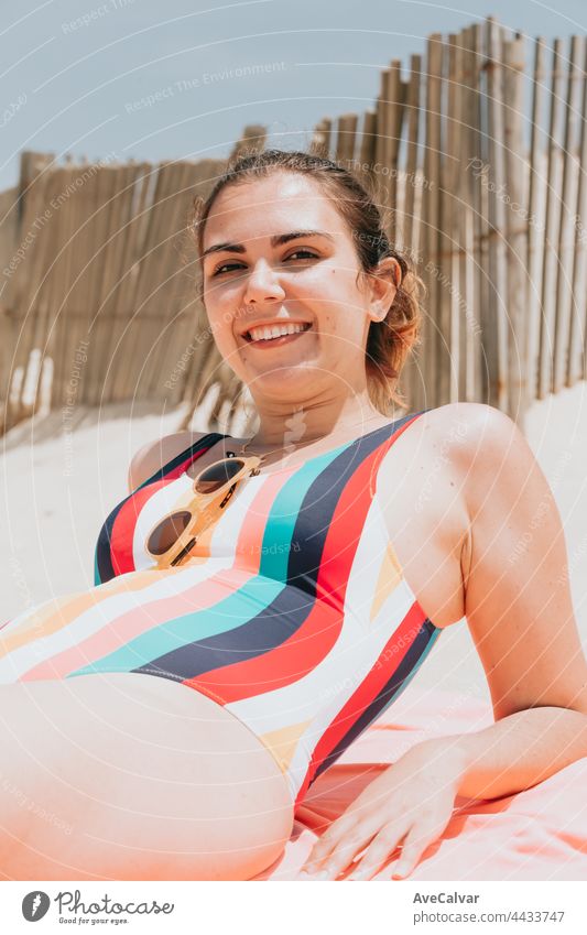 Junge Frau lächelt in die Kamera, während sie einen farbenfrohen Badeanzug am Strand trägt, Reise junges Urlaubskonzept, Kopierraum, soziales Netzwerk, Sonnenbrille Benutzerkonzept