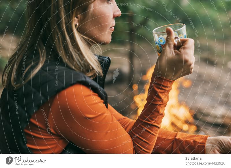 Nahaufnahme einer erwachsenen Frau, die mit einer Tasse Tee am Feuer sitzt und sich im Wald entspannt Camping trinken Sitzen jung Natur Tourist Abenteuer Urlaub