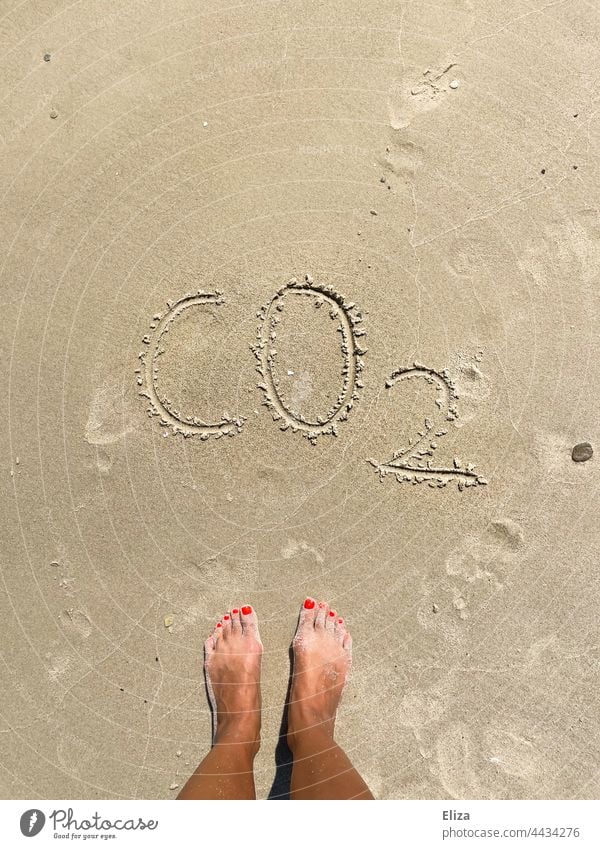 Füße im Sand vor dem Wort CO2 - Konzept Klimakrise und Reisen Kohlenstoffdioxid CO2-Ausstoß Urlaub CO2-Emission Strand Meer co2-Belastung Klimawandel