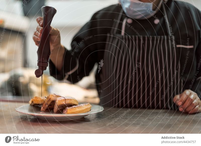 Crop anonymer Koch dekoriert belgische Waffeln mit Schokoladensauce Küchenchef dekorieren Dessert Leckerbissen Mann süß vorbereiten Flasche gebacken Beeren reif