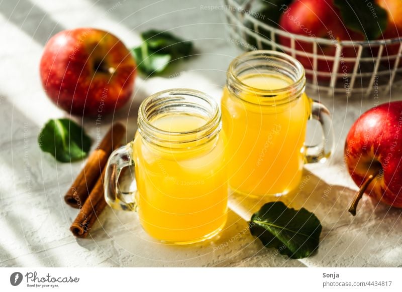 Frischer Apfelsaft in zwei Gläser und rote Äpfel auf einem weißen Tisch Saft Glas Getränk Erfrischungsgetränk Frühstück lecker trinken Innenaufnahme Limonade