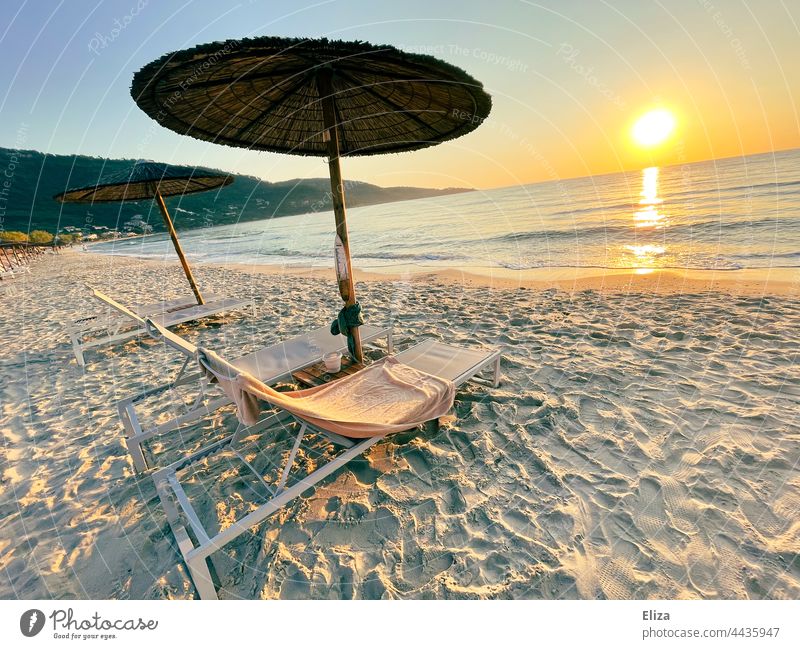 Liegestühle mit Sonnenschirmen am leeren Strand bei Sonnenaufgang Sommer Urlaub Meer Urlaubsstimmung Sandstrand morgens Menschenleer Erholung Himmel Landschaft