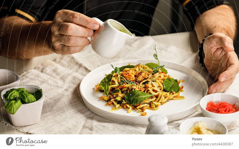Spaghetti mit Meeresfrüchten. Die Hände des Chefkochs bereiten eine traditionelle Pasta mit Meeresfrüchten zu. Der Koch gießt die Soße über das Gericht. Restaurant serviert Gericht. Mediterrane Küche Banner