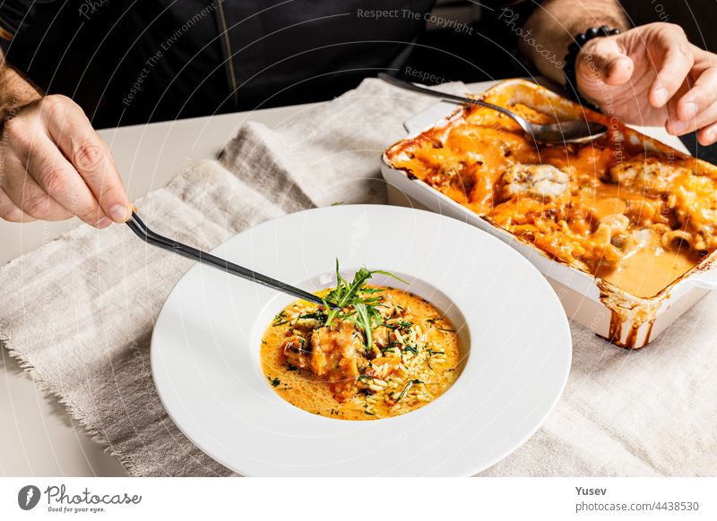 Authentische spanische Paella mit Kabeljau und Muscheln. Ein traditionelles mediterranes Gericht mit Meeresfrüchten. Der Koch dekoriert das Gericht mit einer Pinzette mit Kräutern. Servieren eines Gerichts im Restaurant. Menschen bei der Arbeit. Körperteile