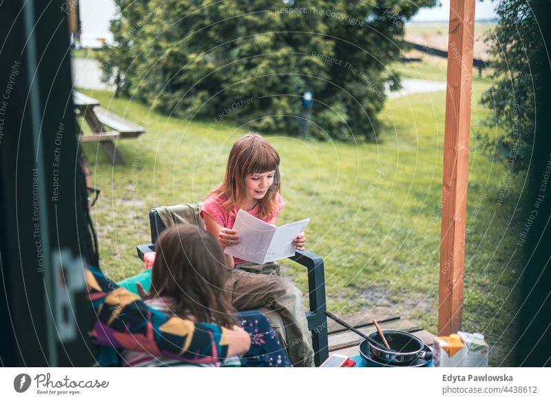 Mädchen beim Lesen vor der Holzhütte auf dem Campingplatz echte Menschen authentisch lesen Mutter Eltern Zusammensein Liebe hölzern Kabine Haus Kinder Familie