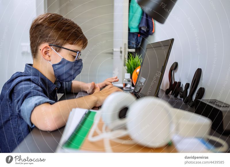 Teenager mit Gesichtsmaske macht Hausaufgaben mit Laptop Schule zu Hause Coronavirus Heimunterricht E-Learning Junge covid-19 Sperrung Schutzmaske Brille Tippen