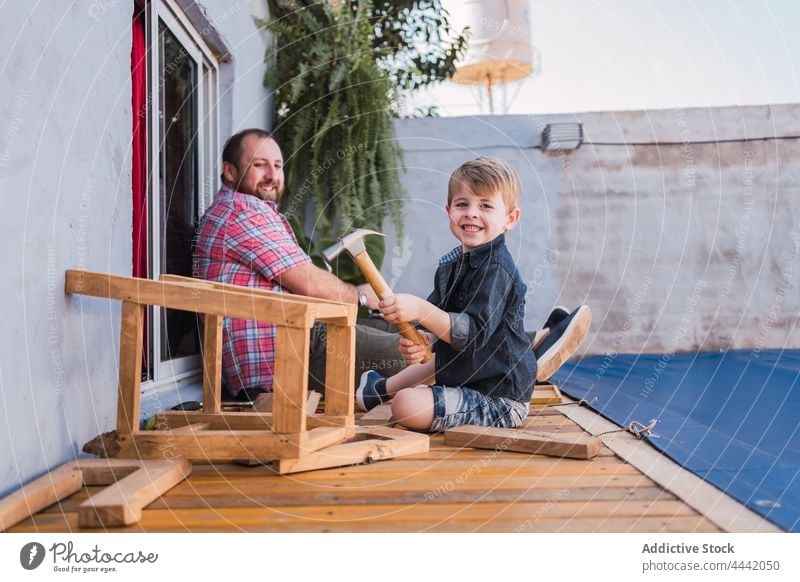 Vater lehrt Junge, wie man mit Holz arbeitet Papa Sohn Holzarbeiten erklären zeigen Hammer heiter Handarbeit diy froh Basteln achtsam Lächeln Freude Mann