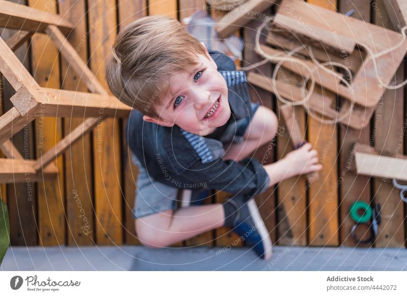 Kleiner Junge auf der Strandpromenade mit Holzteilen Kindheit Starrer Blick Beine gekreuzt handgefertigt hölzern Spielfigur charmant Promenade Porträt Klotz