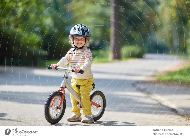 Zufriedenes Kind auf einem Balance-Bike mit einem Helm. An einem sonnigen Sommertag. Gleichgewicht Schutzhelm Sport Kleinkind Fahrrad Baby Park wenig Glück Spaß