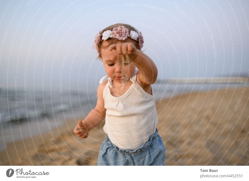 Mädchen mit Blumen in den Haaren spielt am Strand mit Sand - die Zeit rieselt durch die Finger Baby Kleinkind Kind Hand Gesicht 0-12 Monate Auge Blick