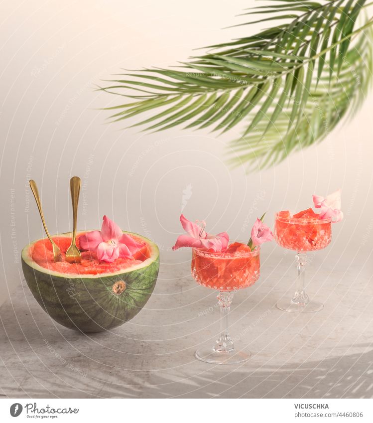 Leckere Wassermelonen-Cocktails in Gläsern mit einer halben Wassermelone, die mit Blumen verziert ist. Sommerliche Erfrischungsgetränke geschmackvoll Brille