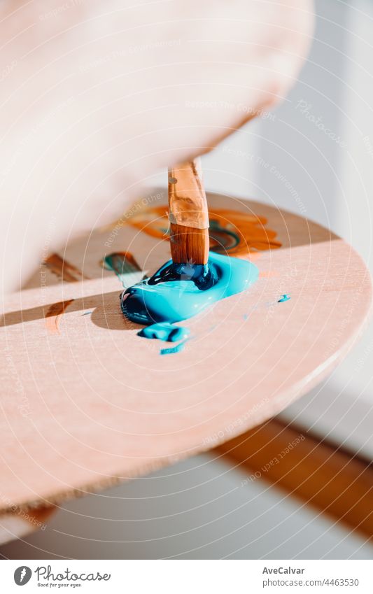 Nahaufnahme eines Pinsels, der blaue Farbe aus einer Künstlerpalette aufnimmt. Buntes Bild aus einem Künstleratelier oder einer Schule mit kreativer Ausbildung