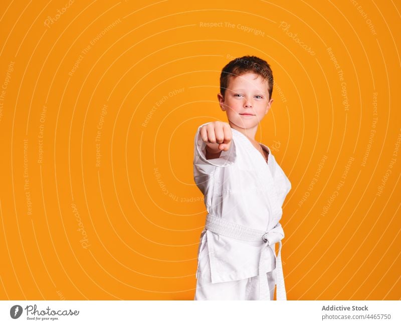 Selbstbewusster Karate-Junge beim Schlag im Studio Bowle selbstbewusst Sport Kraft Kimono Starrer Blick stark Verteidigung Kind Training Kämpfer ernst