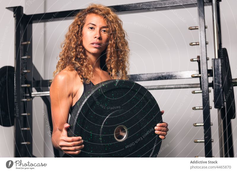 Muskulöse Sportlerin, die im Fitnessstudio eine Hantel auf eine Platte legt hispanisch Mischrennen Teller Curl-Hantel Training Gewicht stark muskulös Frau