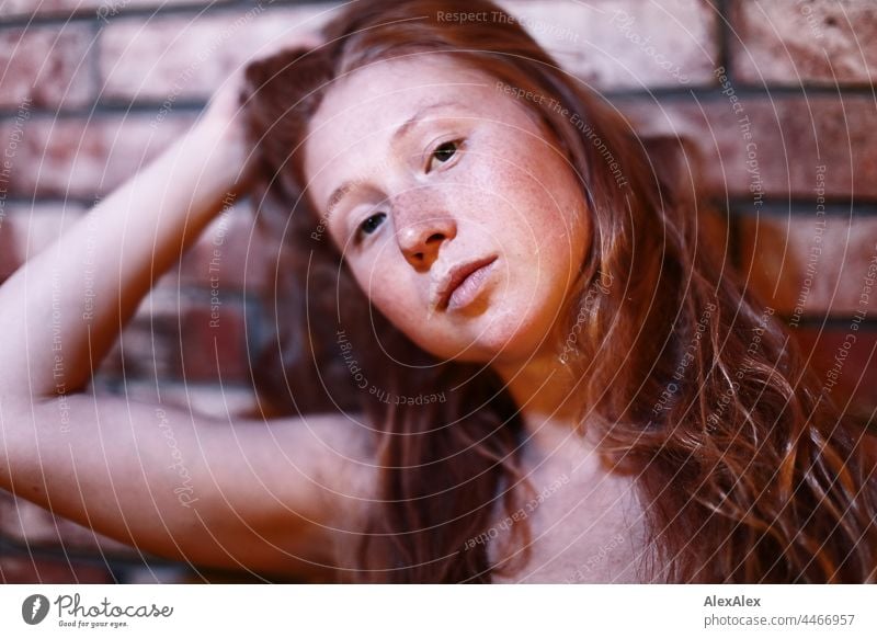 Junge, rothaarige, sommersprossige Frau hält ihre langen Haare nach hinten hoch und schaut seitlich in die Kamera langhaarig sommersprossen Porträt rotblond