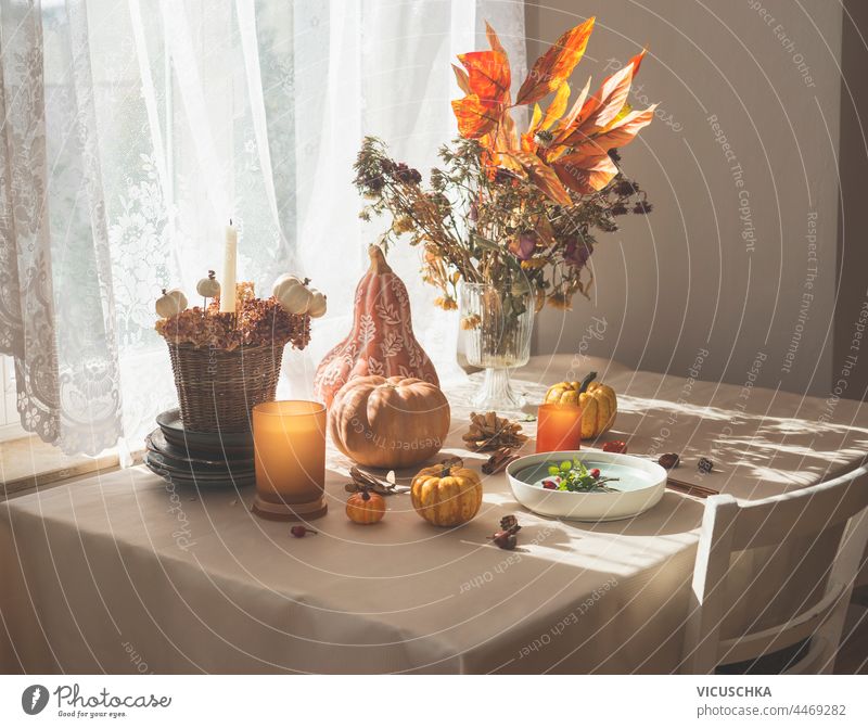 Herbstlich dekorierten Küchentisch mit verschiedenen Kürbisse, Kerzen, Blumen und Herbstblätter Anordnung, Teller und Besteck. Morgendliches Sonnenlicht aus dem Fenster. Häusliches Stillleben
