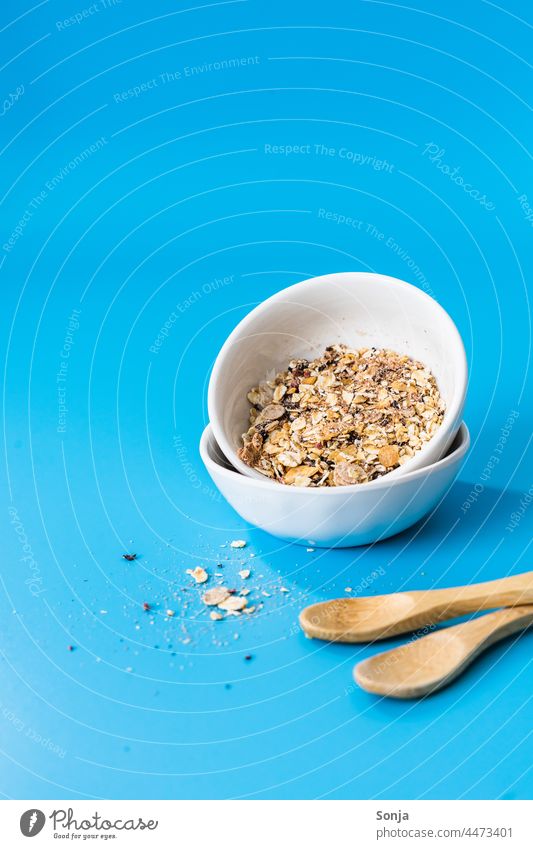 Frühstücksflocken in zwei Schüsseln auf einem blauen Hintergrund. Müsli Hintergrund neutral Löffel Lebensmittel Haferflocken getrocknet Diät Ernährung