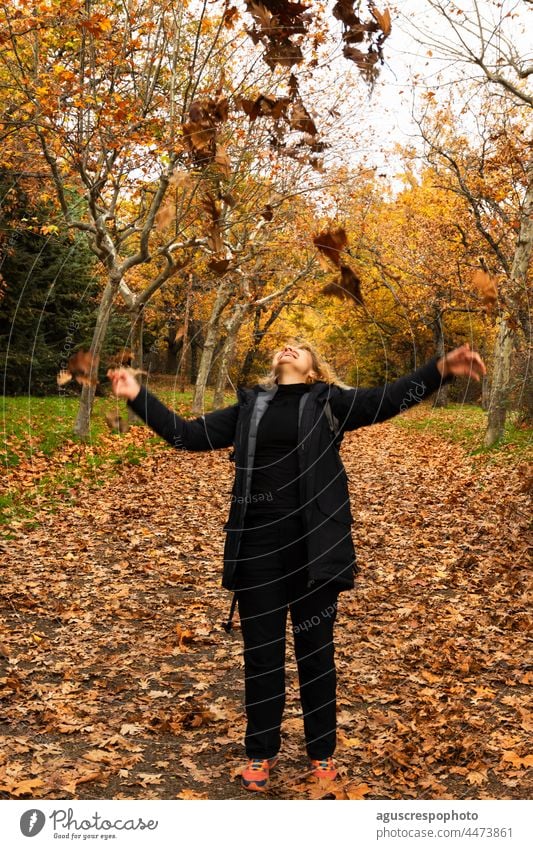 Unbekannte Frau, die lachend Laub in die Luft wirft Wald Herbst Hintergrund Blätter ocker braun golden gelb orange fallen Farben Wandel & Veränderung Baum Zweig