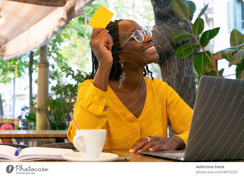 Gut gelaunte schwarze Frau mit Kreditkarte und Laptop freiberuflich Café online Internet Zahlung Kauf kaufen Kaffee Tisch Kantine Tasse Netbook abgelegen