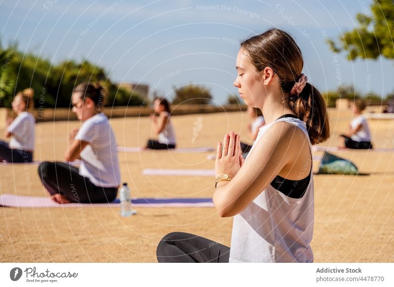 Frau im Lotussitz mit Namaste-Händen während der Yoga-Praxis Windstille Lotus-Pose padmasana üben Wellness Sportkleidung Asana jung Barfuß Unterlage Brille