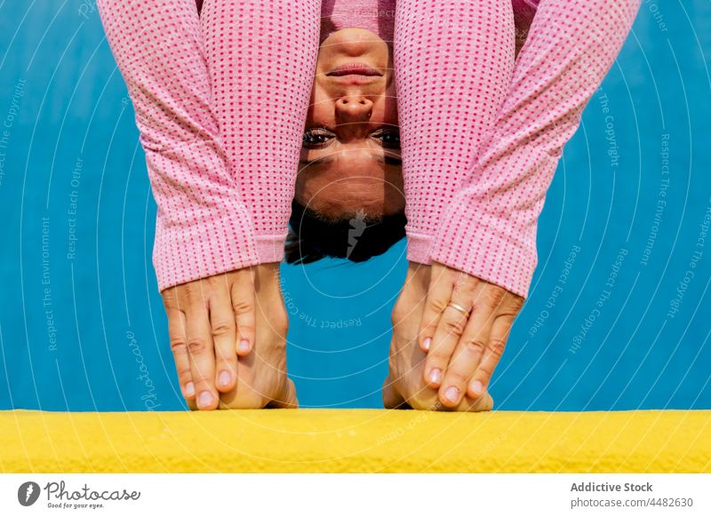 Frau in hellrosa Sportkleidung in Kopf-an-Knie-Pose Yoga üben beweglich Dehnung Asana uttanasana Vorwärtsbeuge Wellness Wohlbefinden Wegbiegung gelb blau ruhig
