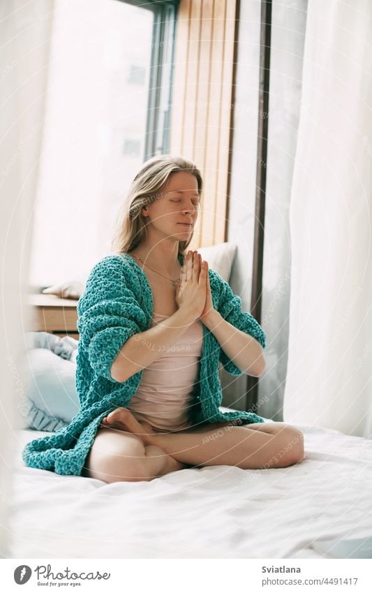 Ein junges Mädchen meditiert in der Lotus-Position auf dem Bett im Schlafzimmer. Das Mädchen macht Anti-Stress-Yoga am Morgen zu Hause Meditation Frau Lotos