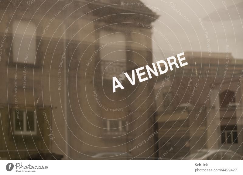 Spiegelung einiger Wohnhäuser in einem Schaufenster mit Aufschrift a vendre text zu verkaufen Wohnhaus Gedeckte Farben grau Schrift französisch Frankreich