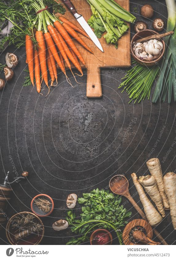 Lebensmittel Hintergrund mit verschiedenen Gemüse und Zutaten: Karotten, Pilze, Pastinaken, Knoblauch, Küchenutensilien auf dunklen Betontisch. Kochen mit gesundem Gemüse der Saison. Draufsicht mit Kopierbereich