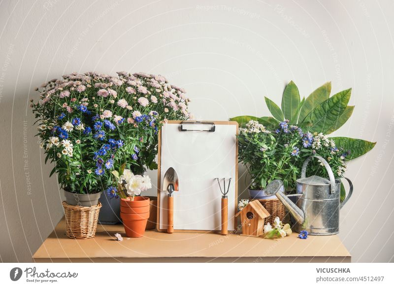 Gartentisch mit leerer To-Do-Liste, Gartengeräten und Topfblumen Gartenarbeit Tisch Aufgabenliste Gerät eingetopft weiß Wand Hintergrund Vorderansicht