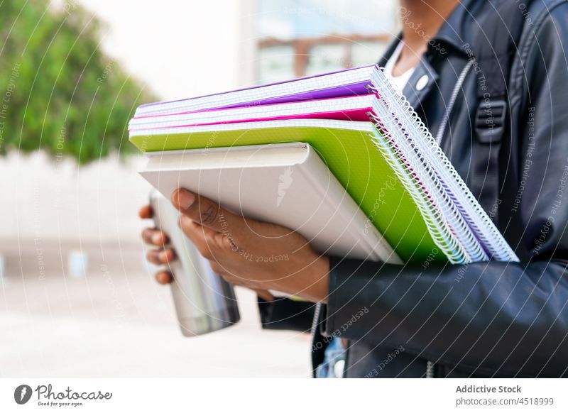 Anonyme schwarze Frau mit Schulheften auf dem Campus Schüler Straße Universität Bildung Wissen Thermoskanne Schönschreibheft lernen Lehrbuch Getränk Heißgetränk