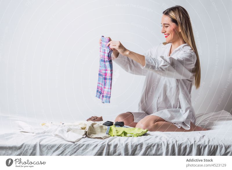 Schwangere Frau in weißem Hemd bereitet Babykleidung vor schwanger Pferch Stoff erwarten pränatal vorwegnehmen vorbereiten Schwangerschaft zerknittern Kind