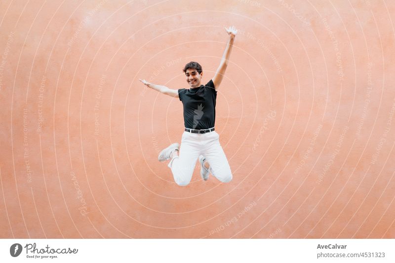 Junger Mann in urbaner Kleidung, der vor einer massiven orangenen Wand fällt und springt, Copy Space, Werbebild, Freiheitskonzepte, Stadtleben, Leben in der Stadt, Abenteuerkonzept, lgbt