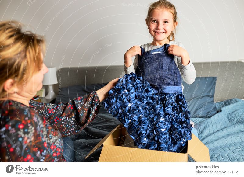 Mutter und ihre Tochter öffnen die Schachtel mit dem bestellten Kleid. Online-Shopper Kunde hält Kleid online kaufen Auspacken Orden Geschenk präsentieren