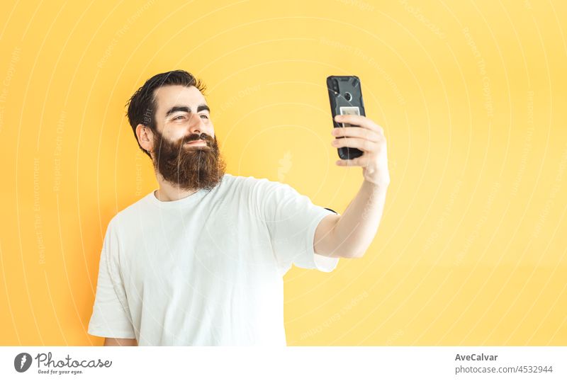 Junge Hipster bärtigen Mann, der ein Selfie auf seinem Handy, leeren Raum, Kopie Raum, weichen gelben abnehmbaren Hintergrund, minimal basic, Ad-Konzept Deal, weißes Hemd Raum