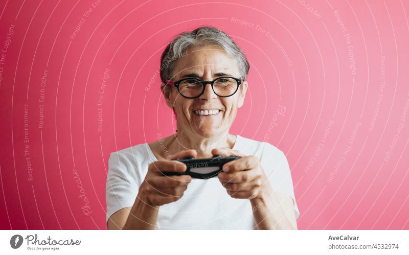 Alte ältere Frau lächelnd in die Kamera, während sie eine Konsole Pad, Videospiele spielen pastellrosa abnehmbaren Hintergrund, Videospiele alte Menschen, Kopie Raum, weißes Hemd Raum