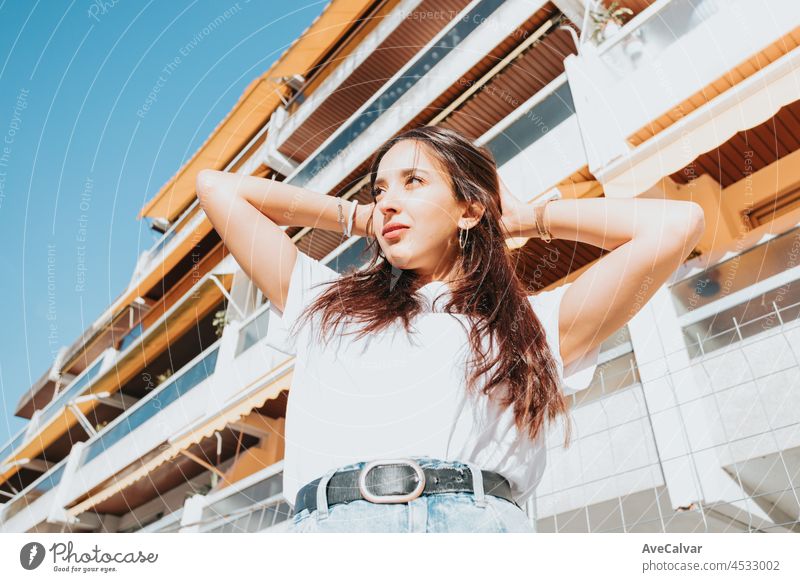 Close up Porträt der jungen arabischen Frau Blick weg von der Kamera weißes Hemd und blaue Jeans lächelnd in die Kamera auf einem Block in der Kapuze. Straße Leben Stil, cool trendy. Soziales Netzwerk Konzept