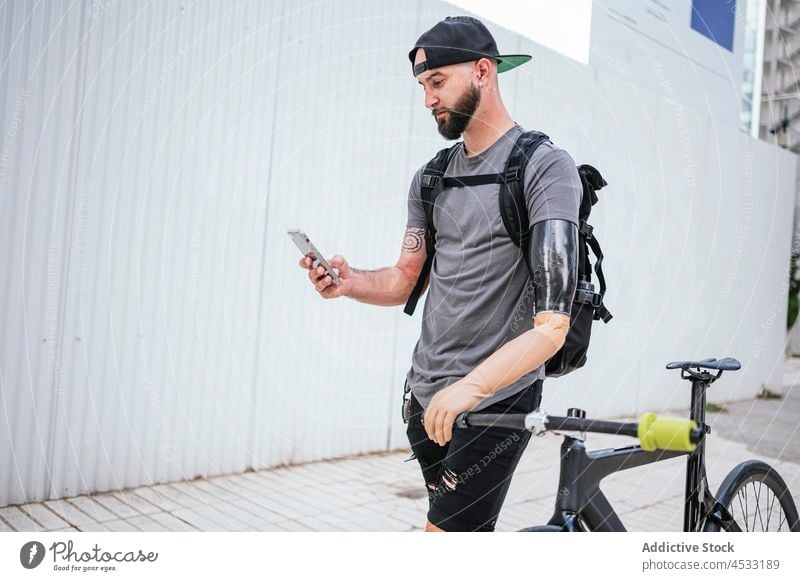 Mann mit Armprothese beim Surfen auf dem Smartphone Arme Prothesen Prothetik Browsen künstlich Glied Amputierte männlich Handicap Gerät Glück stehen Fahrrad